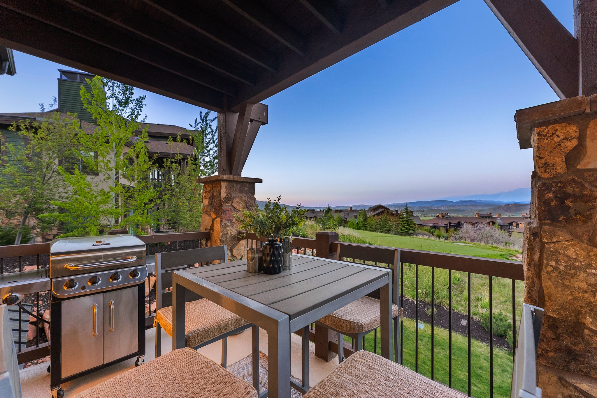 Covered outdoor patio featuring exposed wooden beams, stone-clad columns, and a railing with dark metal pickets