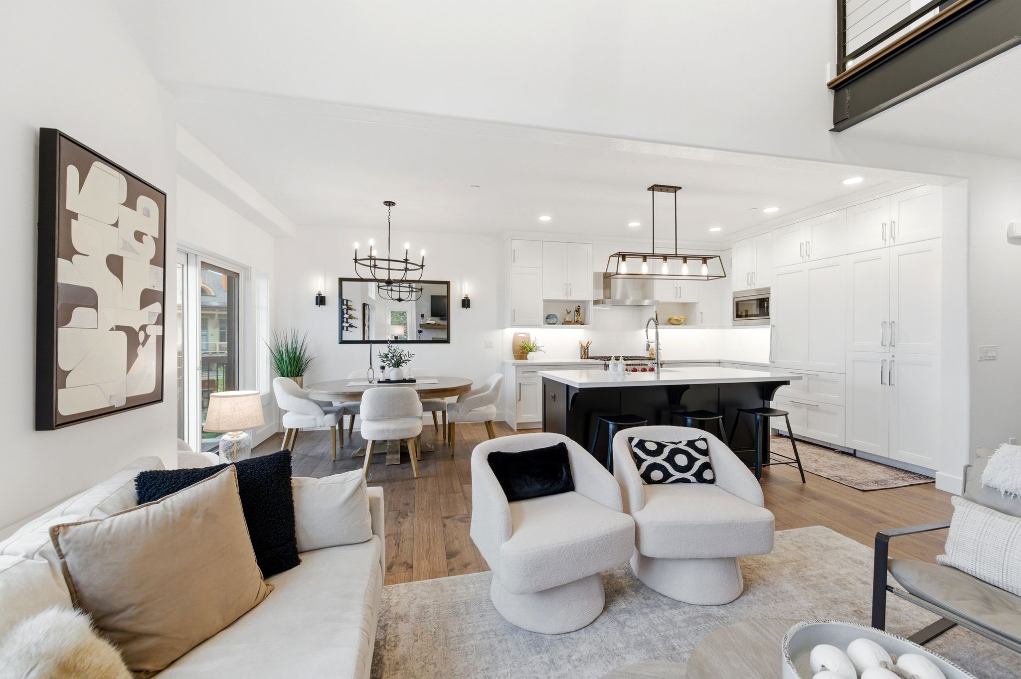 Open-concept living area featuring wood-finish flooring, a contemporary kitchen with a dark island and white cabinetry, a dedicated dining space with a chandelier, and a bright living room with abundant natural light