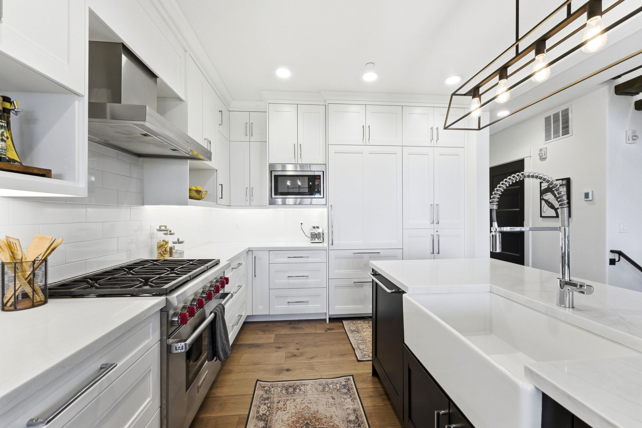 Modern kitchen featuring white cabinetry, integrated appliances, a large farmhouse sink, and wood-finish flooring