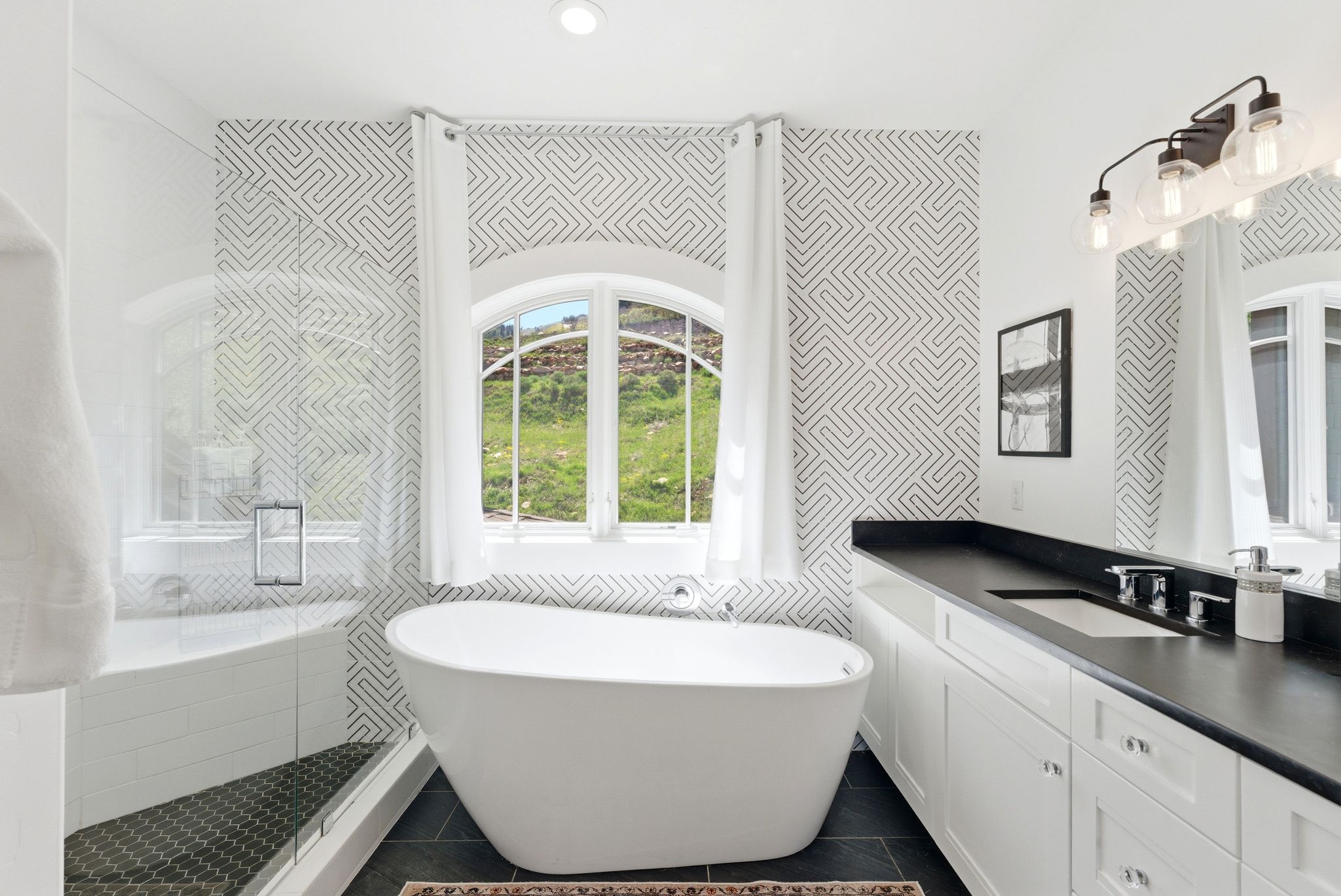 Freestanding soaking tub centered under an arched window with a green landscape beyond