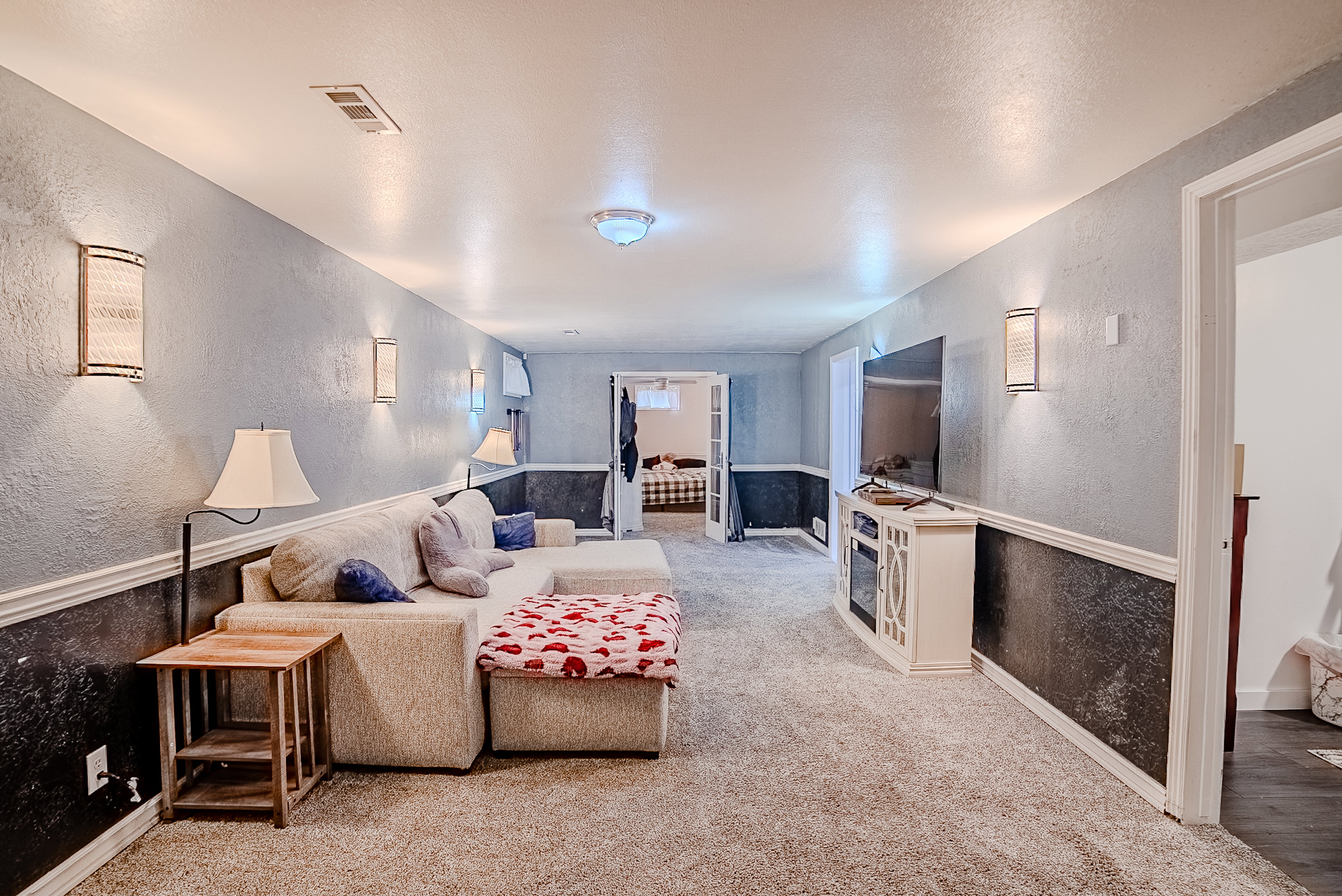 Spacious room featuring light gray textured walls with a dark gray wainscoting accent, recessed ceiling lights, and multiple wall sconces