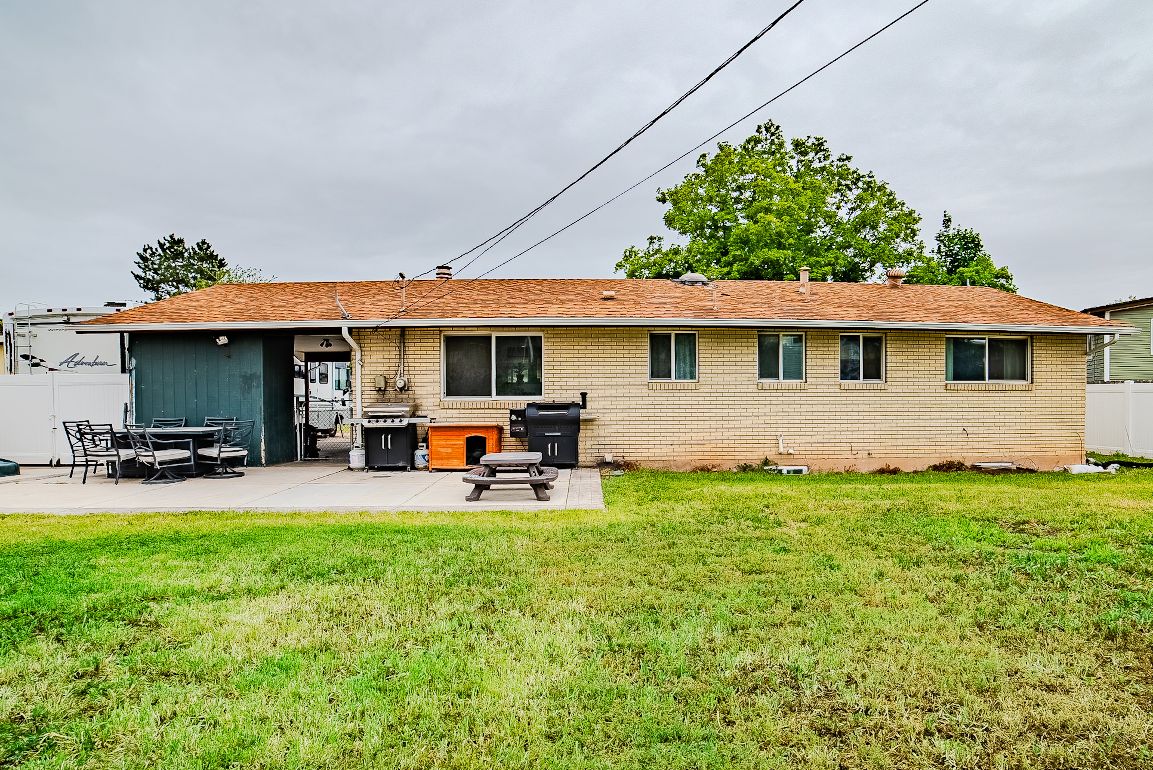 Spacious backyard featuring a large concrete patio, expansive lawn, and brick exterior with multiple windows