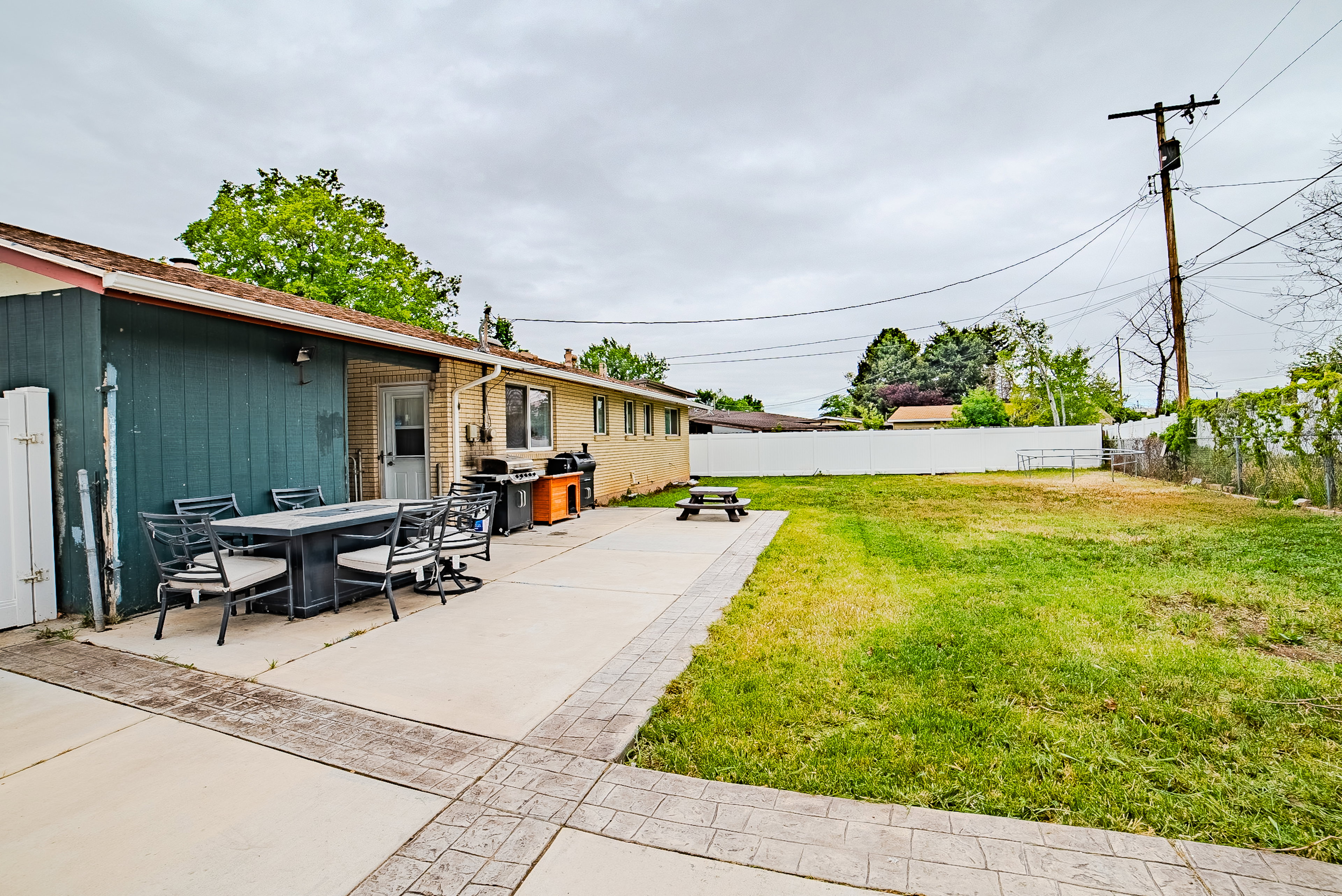 Expansive backyard featuring a concrete patio with stamped border, a large lawn area, and a white privacy fence