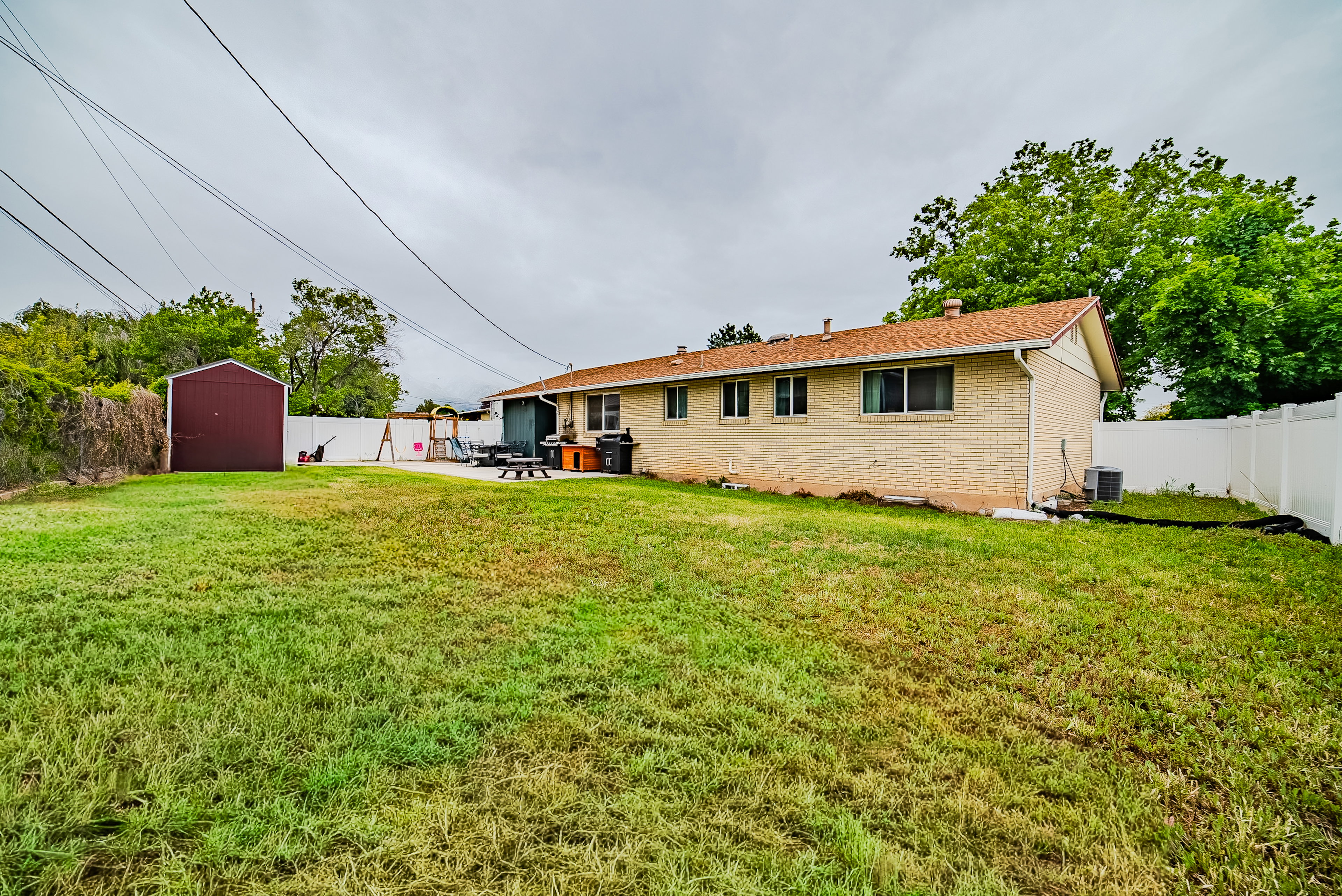 Spacious backyard featuring a large grass area, a dedicated concrete patio, and a utility shed