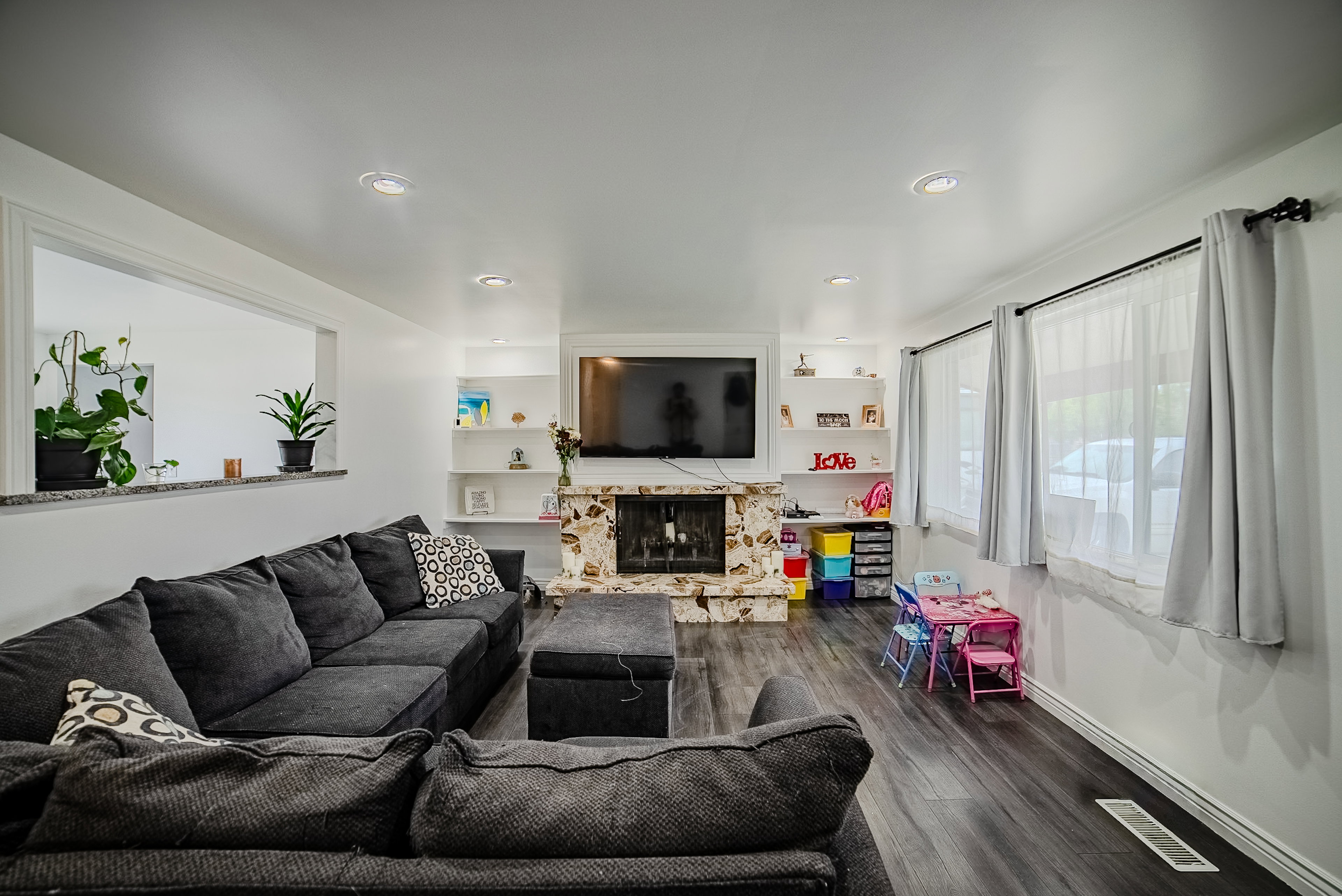 Spacious living area featuring a stone-clad fireplace, wood-finish flooring, recessed lighting, built-in shelving, and multiple windows