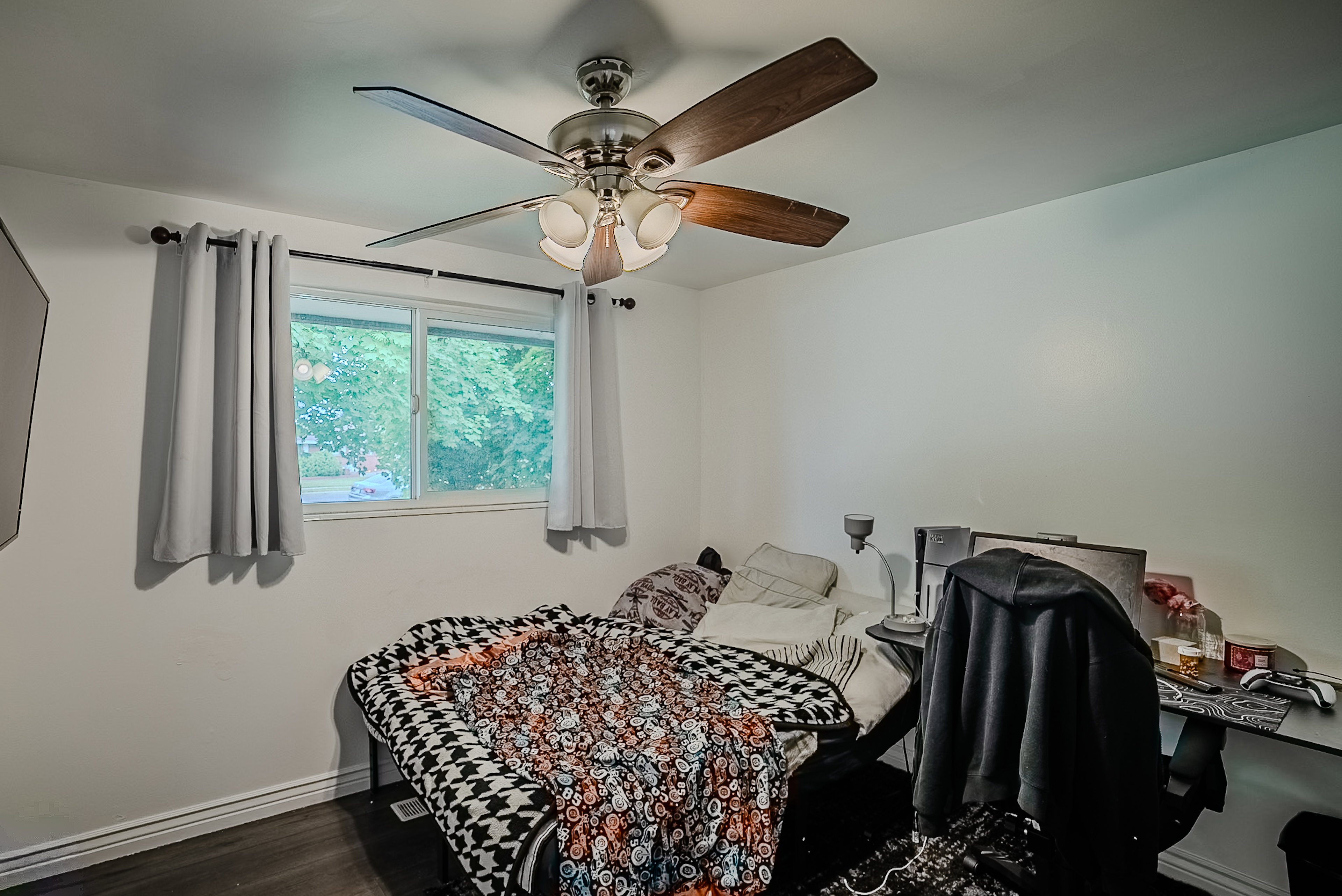Bedroom featuring a ceiling fan with wood-finish blades, a double-pane window, and wood-finish flooring