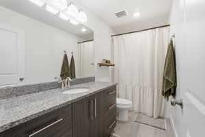 Bathroom featuring a wood-finish vanity with an undermount sink, a stone-finish countertop, and a large wall-mounted mirror