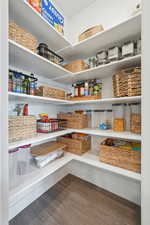 Corner pantry featuring multiple white shelves, wood-finish flooring, and white trim