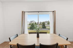 Bright dining area featuring a large window with roller shades and natural wood-finish flooring