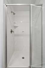 Primary Suite Eenclosed shower with a brushed nickel showerhead and control handle, integrated shelving, and a clear glass door