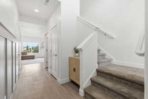 Entryway featuring wood-finish flooring, white board and batten wall paneling, and a carpeted staircase with white railings