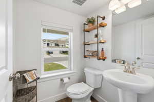 Bathroom featuring a pedestal sink with brushed nickel faucet, a wall-mounted mirror, and an industrial-style shelving unit with wood shelves. Located at bottom of stairs.