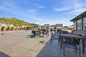 Expansive concrete patio with multiple outdoor dining areas, a nearby pool, and a clubhouse building featuring large windows and stone detailing
