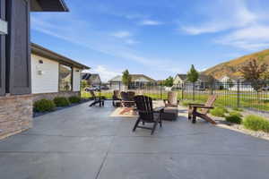 Expansive concrete patio area featuring a stone veneer accent wall, perimeter landscaping with shrubs and decorative rock, and a black metal fence