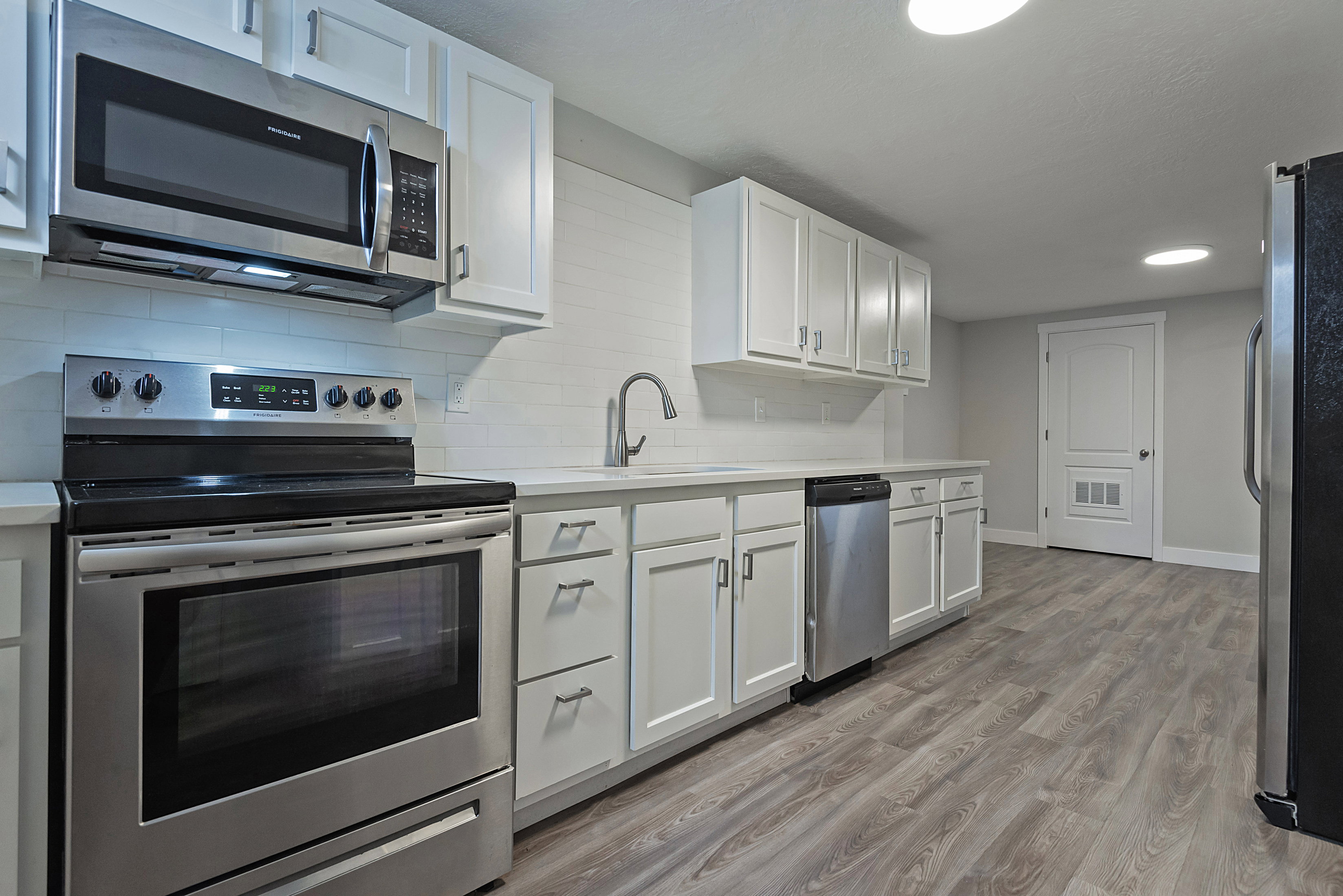 Contemporary kitchen featuring white cabinetry, stainless steel appliances, a tile backsplash, light-toned countertops, and wood-finish flooring