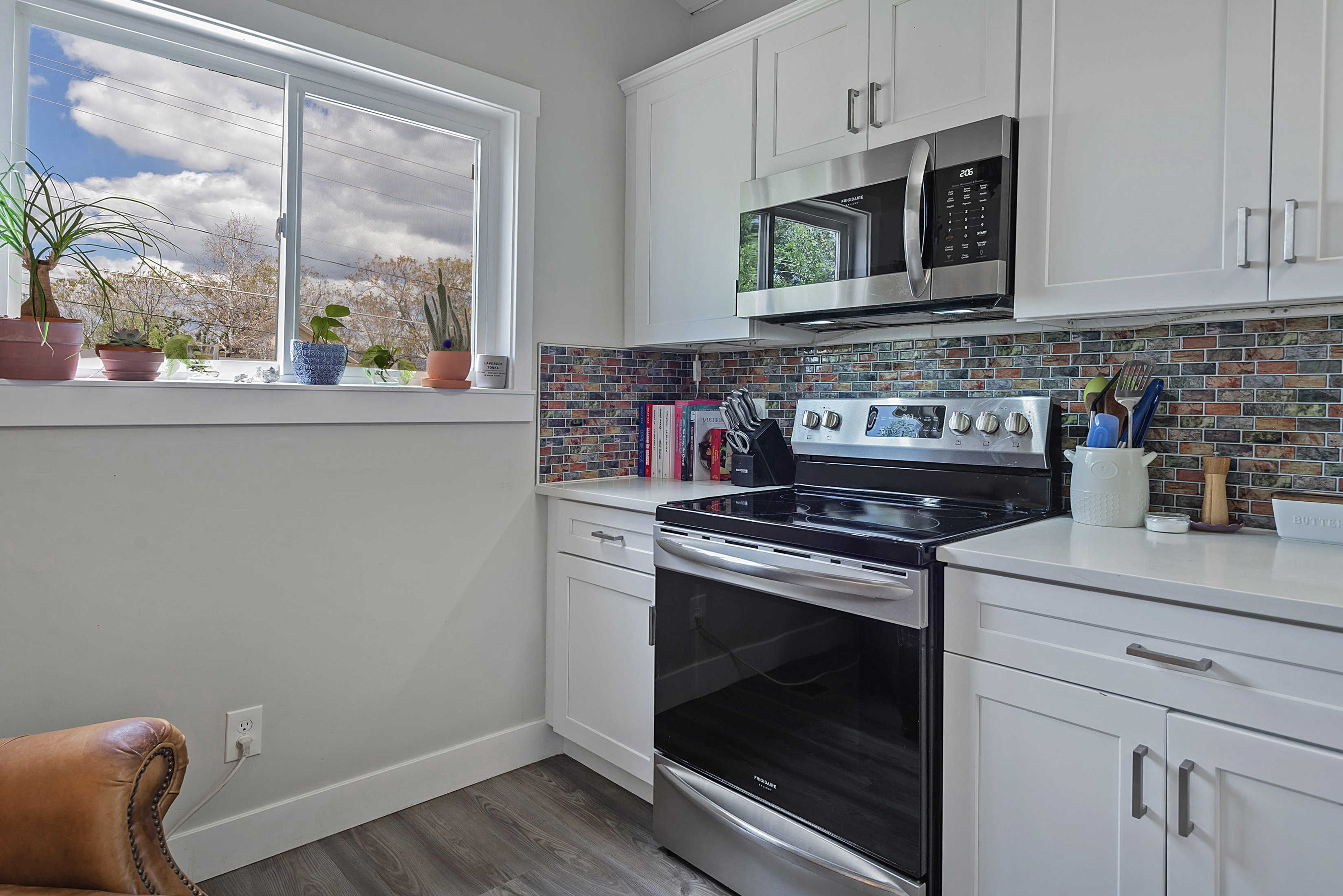 Kitchen featuring stainless steel appliances, white cabinetry with silver hardware, a colorful mosaic tile backsplash, and light countertops