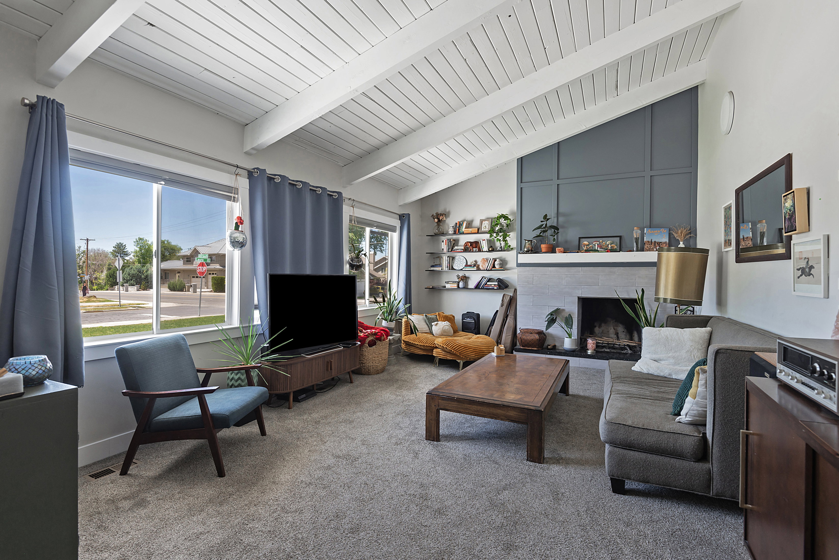 Living area featuring a vaulted ceiling with exposed white beams, large windows, and carpet flooring