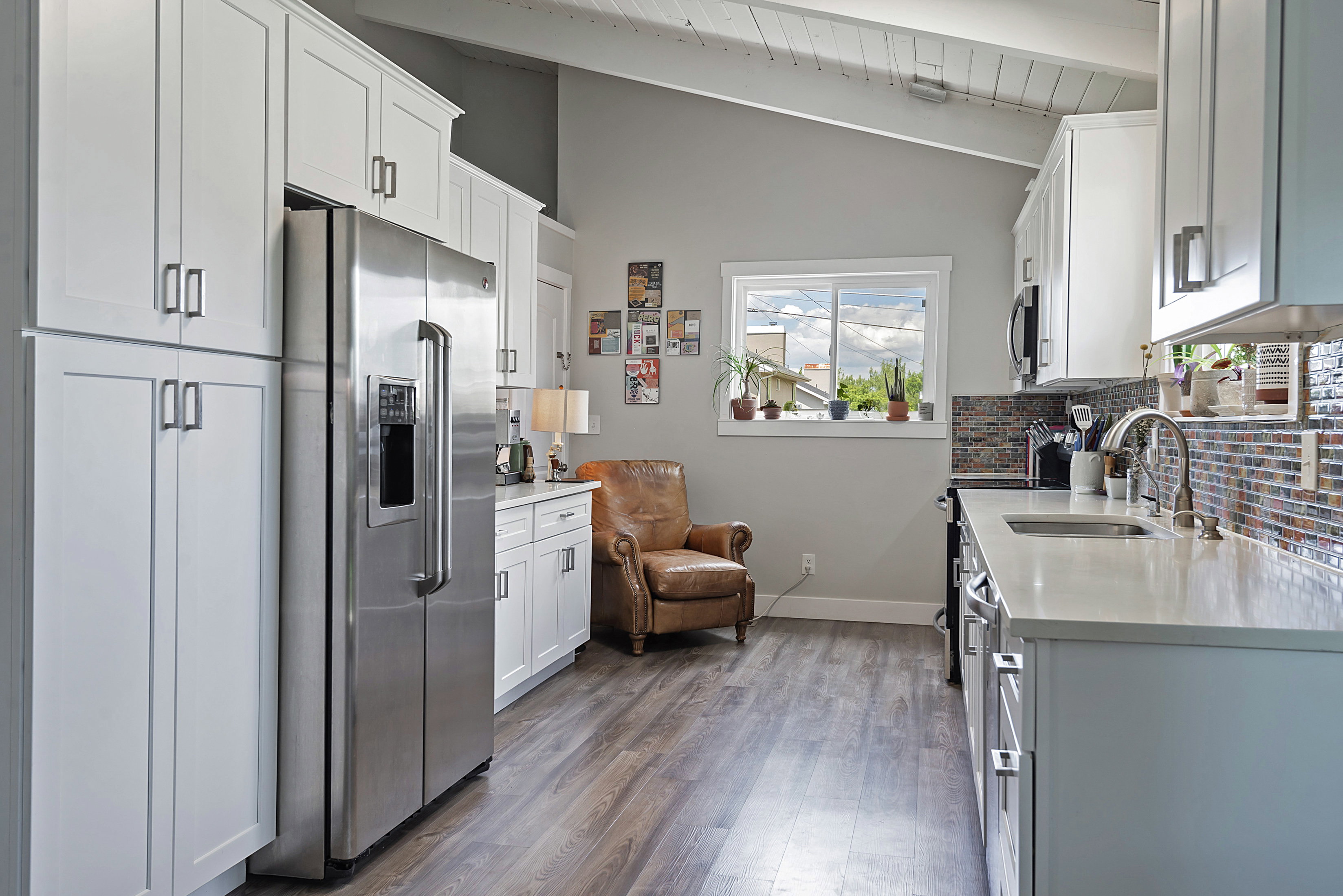 Modern kitchen featuring white shaker cabinetry, wood-finish flooring, a stainless steel refrigerator, light-toned countertops, and a mosaic tile backsplash