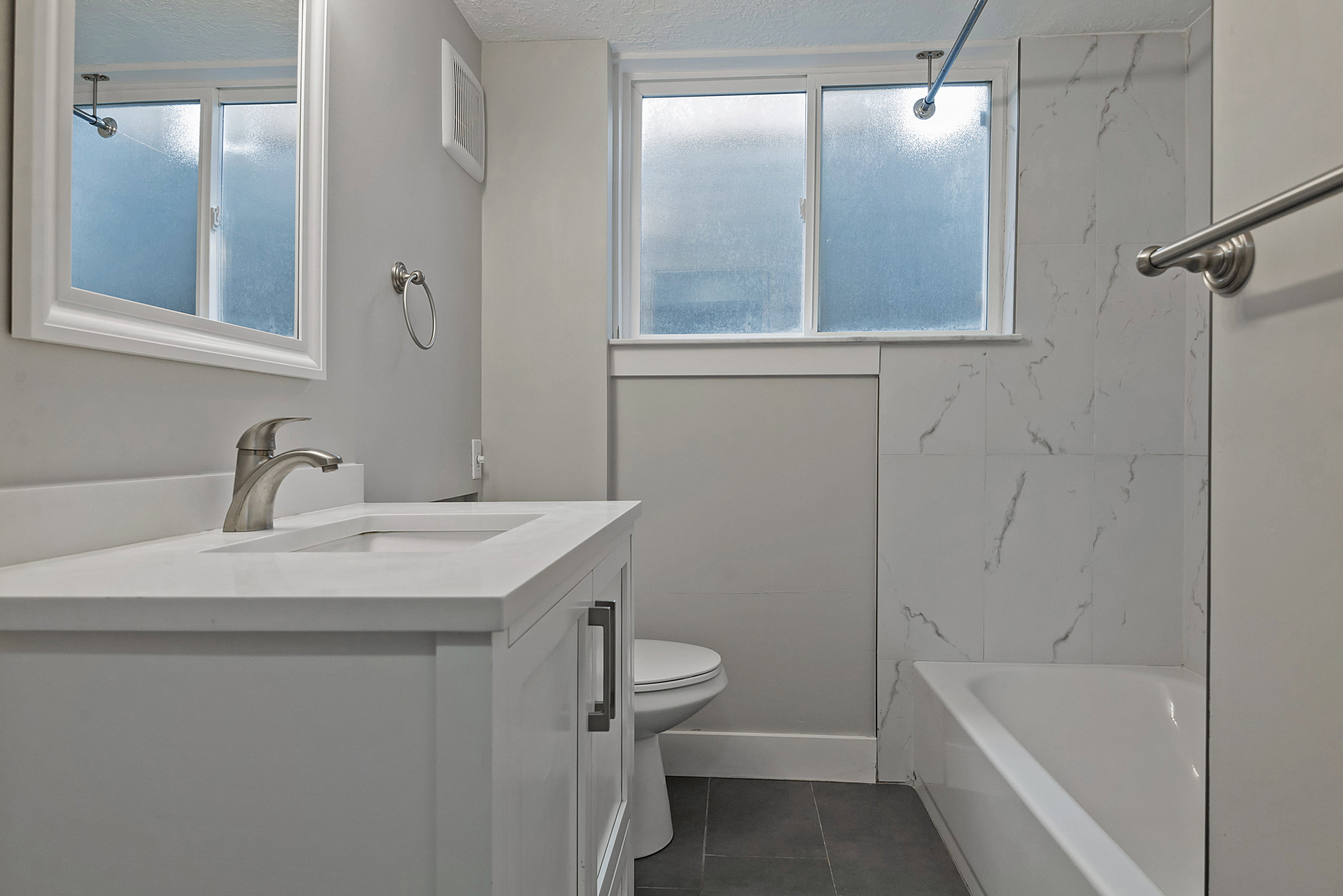 Bathroom featuring a white vanity with an integrated sink, brushed nickel faucet, and a framed mirror