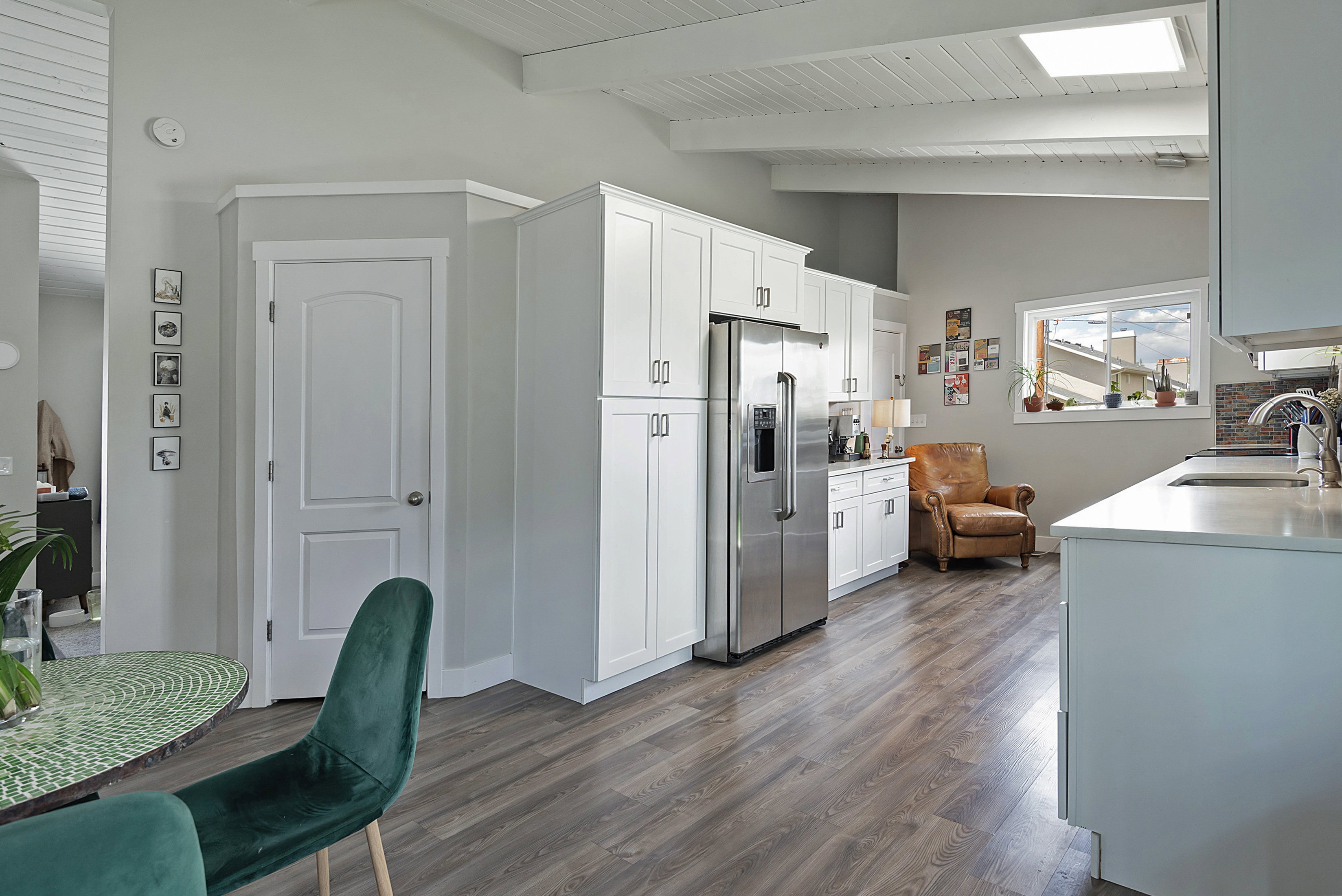 Kitchen featuring white cabinetry, stainless steel refrigerator, wood-finish flooring, a skylight, and an exposed beam ceiling