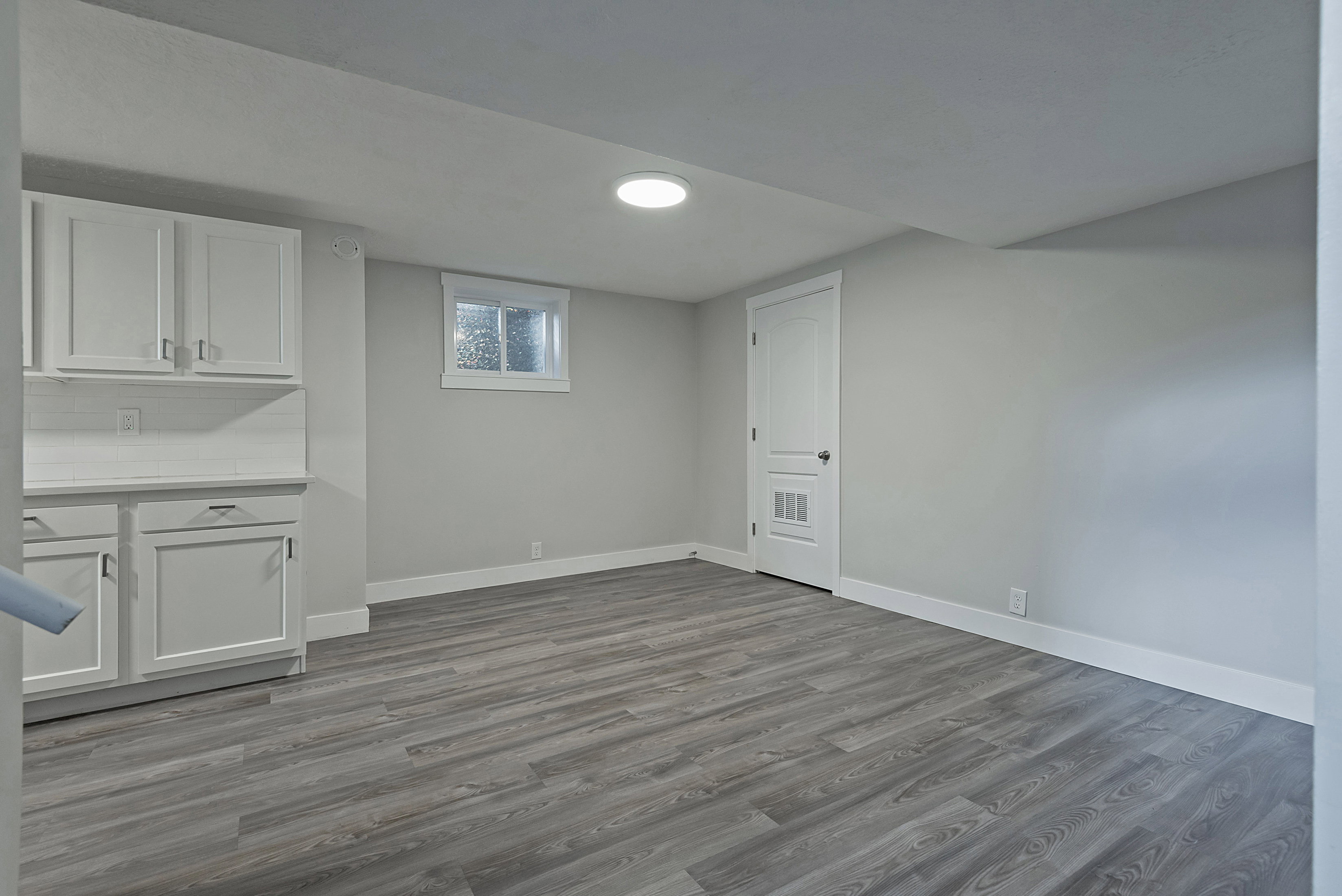 Spacious room featuring wood-finish flooring, light grey painted walls, white baseboards, and a single window