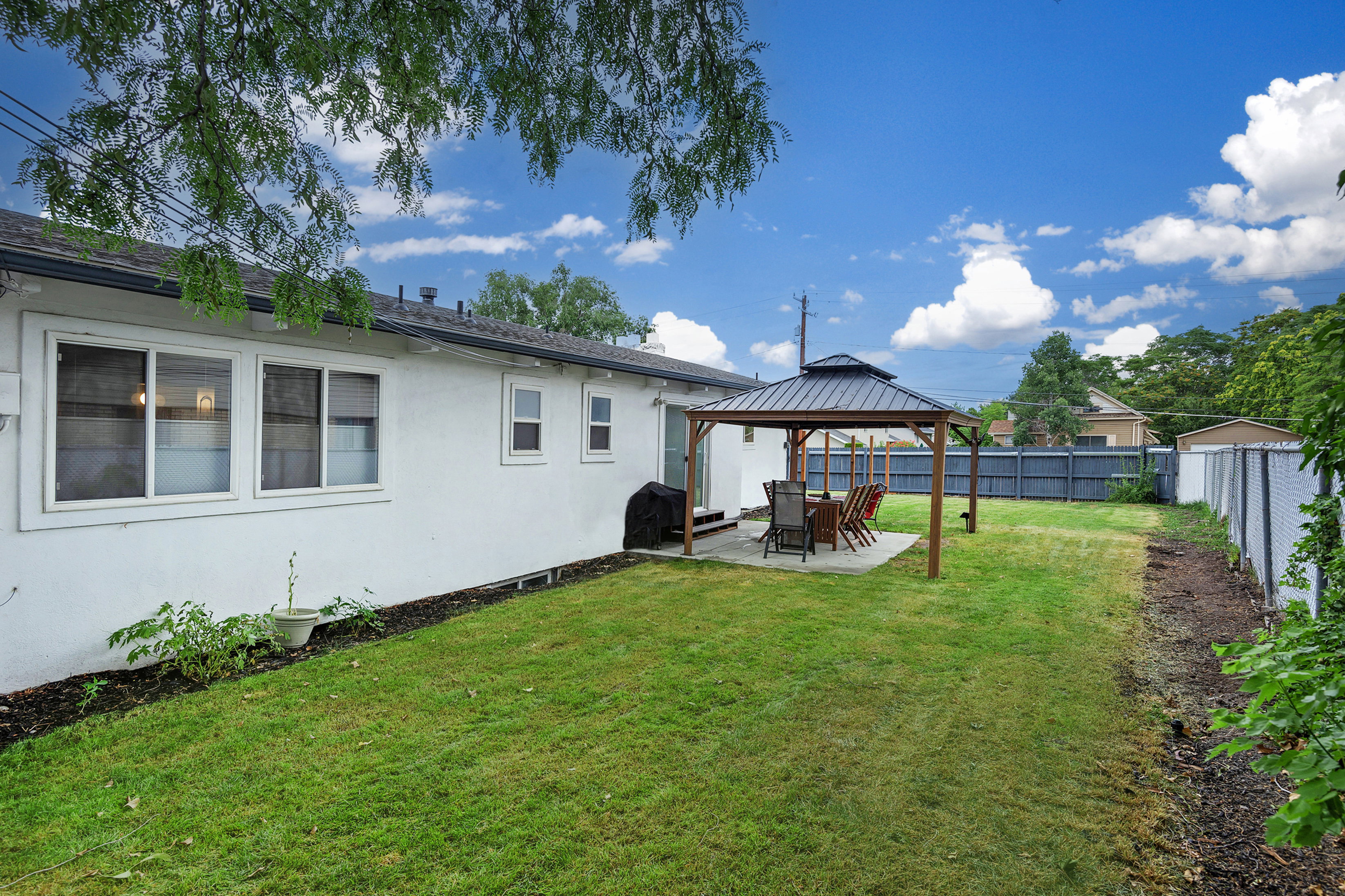 Spacious backyard featuring a covered patio with a dark-frame gazebo, a manicured lawn, and a privacy fence