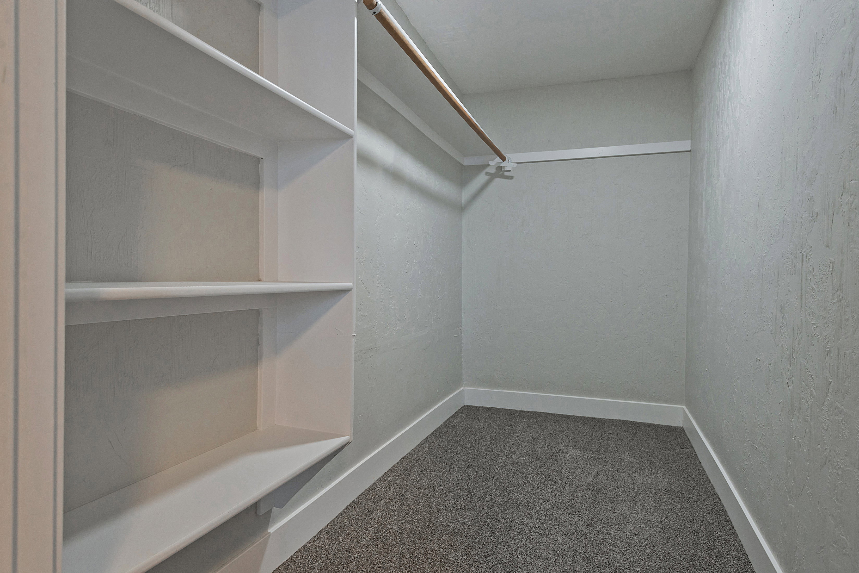 Walk-in closet featuring built-in shelving, a clothes rod, light gray walls, white baseboards, and gray carpet