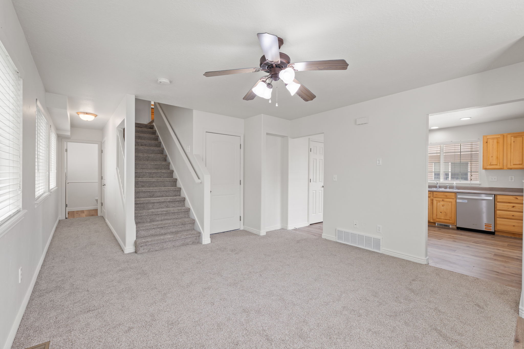 Spacious carpeted living room with fresh neutral paint and abundant natural light, open to the kitchen