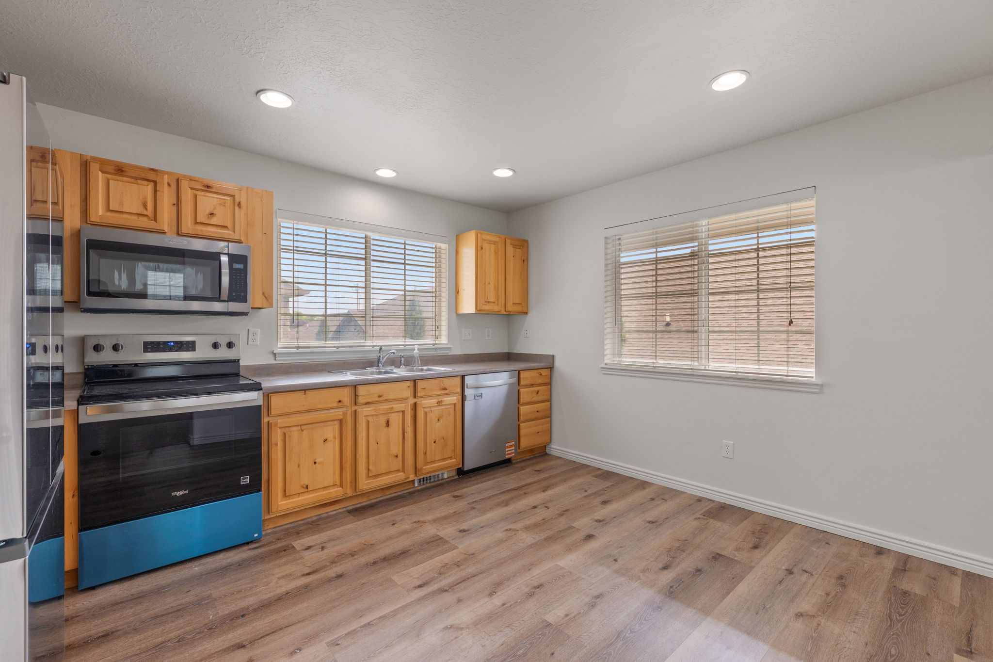 Open eat-in kitchen with natural wood cabinetry, LVP flooring, recessed lighting, and new stainless steel appliances