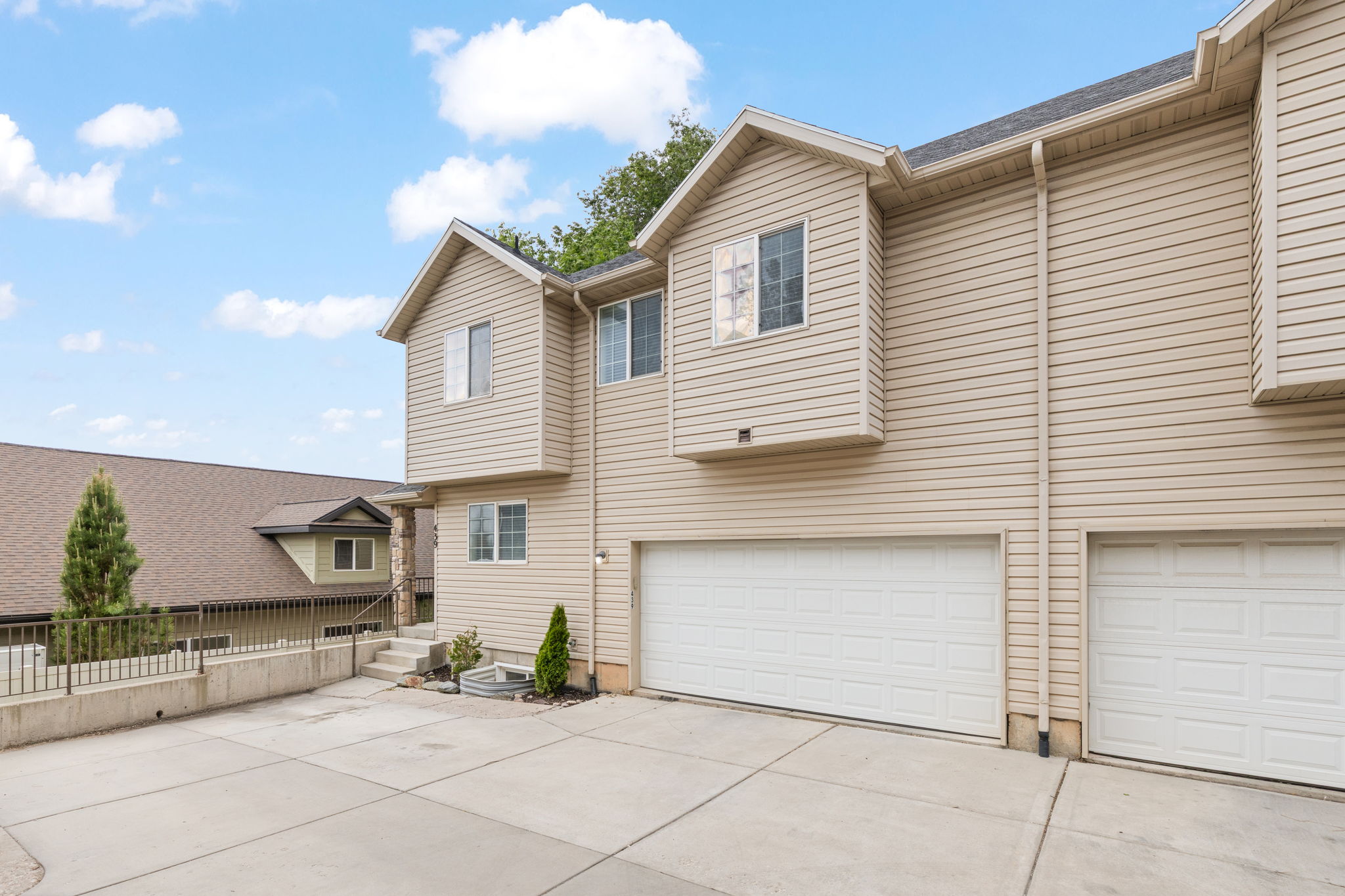End-unit townhome featuring two-car garage, covered front porch, light neutral siding, and mature landscaping