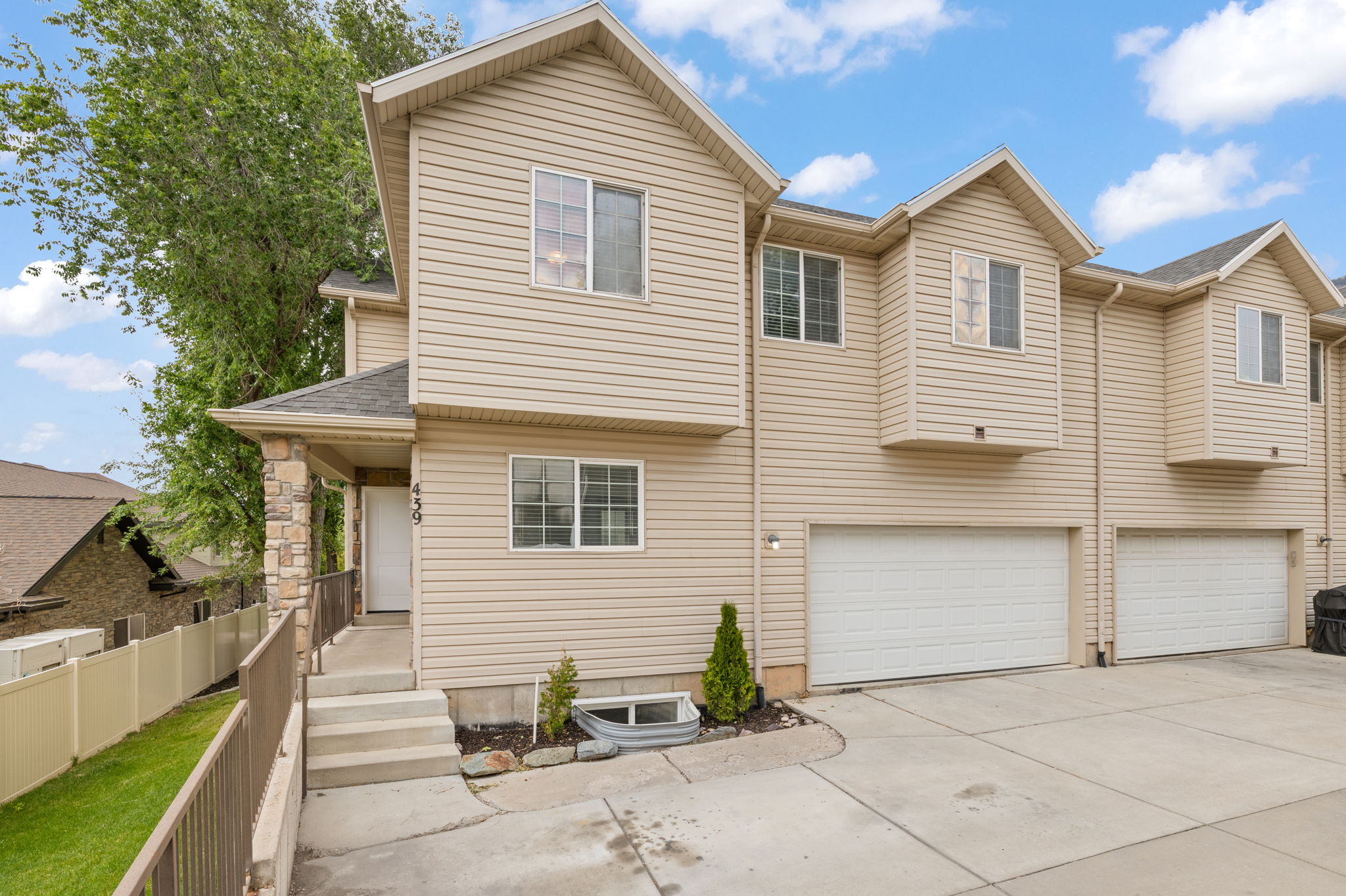 End-unit townhome featuring two-car garage, covered front porch, light neutral siding, and mature landscaping