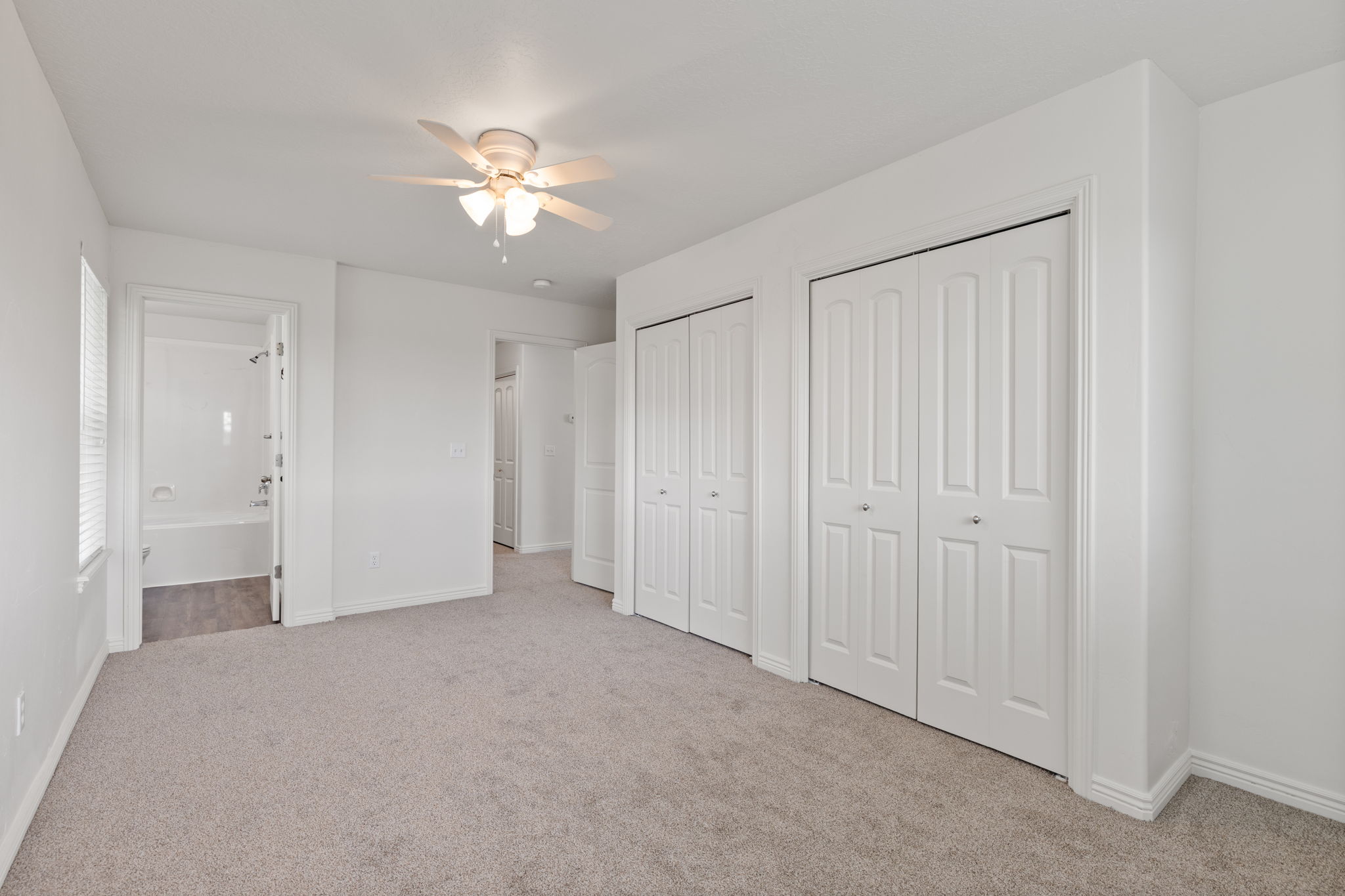 Primary bedroom with brand new carpet and light neutral paint, abundant natural light, double closets, and ceiling fan