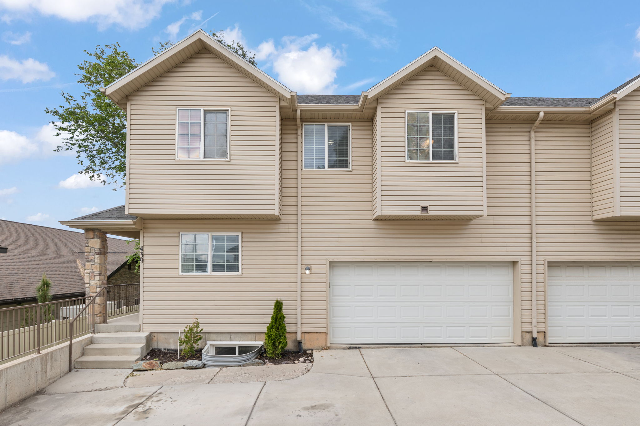 End-unit townhome featuring two-car garage, covered front porch, light neutral siding, and mature landscaping