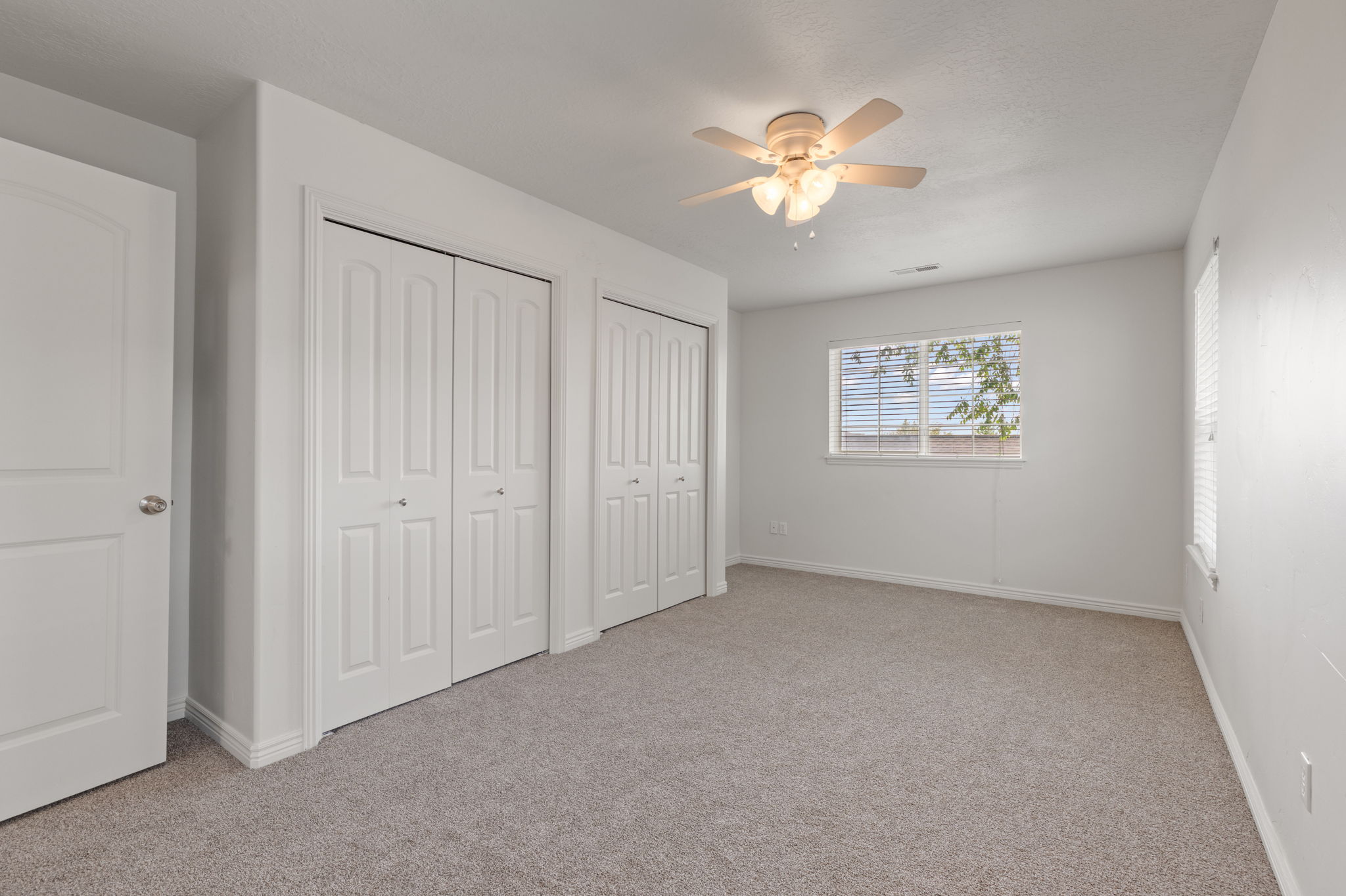 Primary bedroom with brand new carpet and light neutral paint, abundant natural light, double closets, and ceiling fan