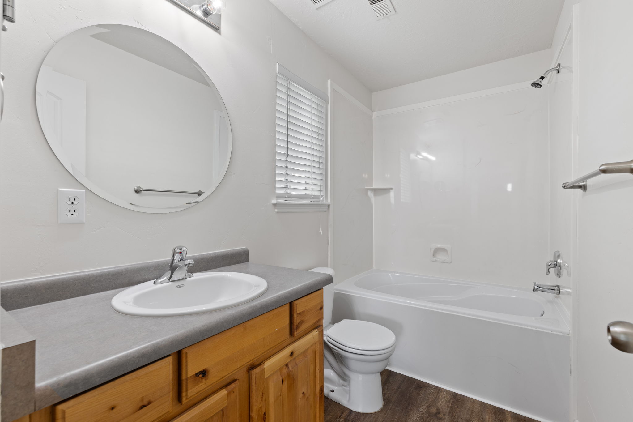 Primary bathroom with spacious vanity, decorative mirror, LVP flooring, and oversized tub/shower combination.