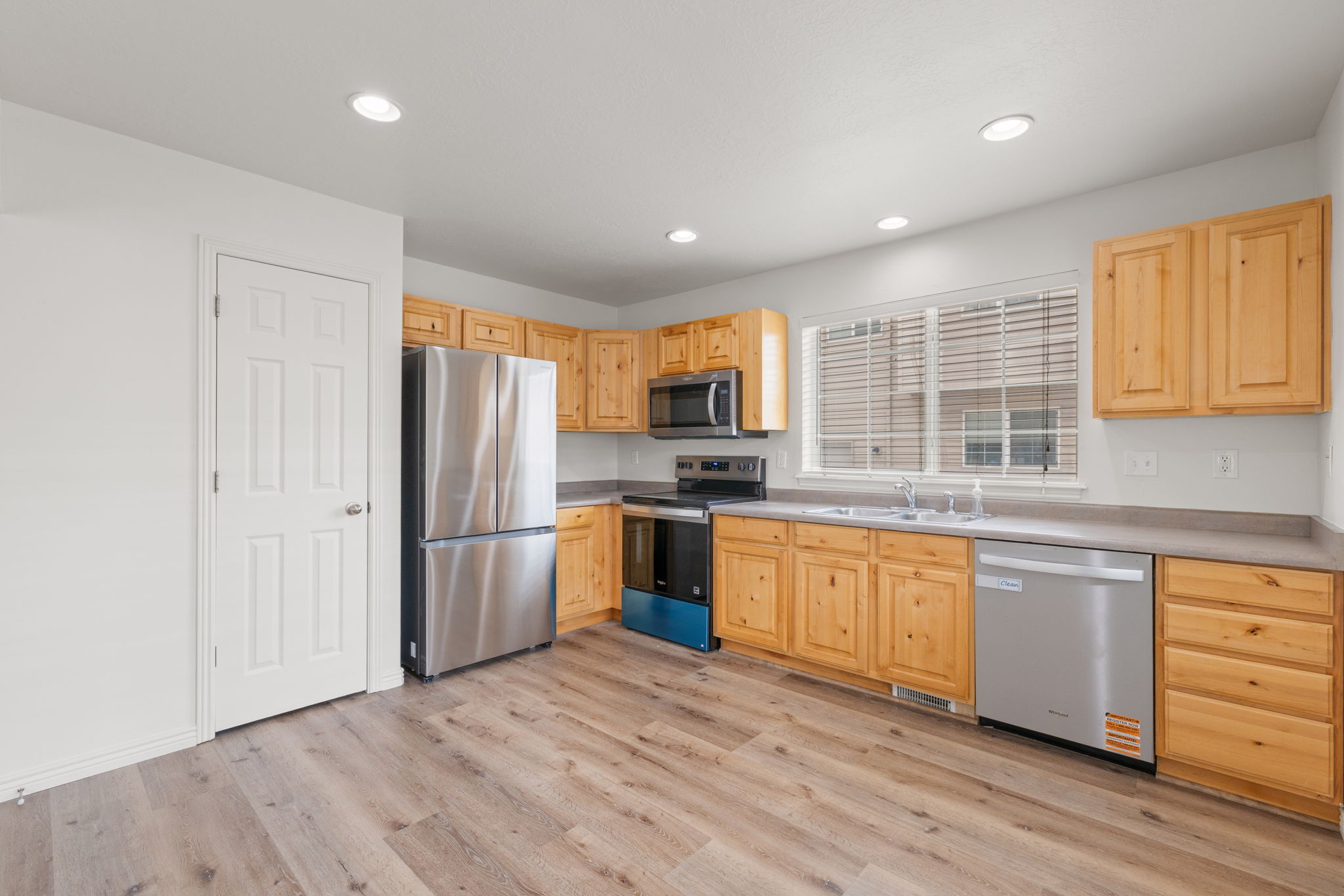Open eat-in kitchen with natural wood cabinetry, LVP flooring, recessed lighting, and new stainless steel appliances