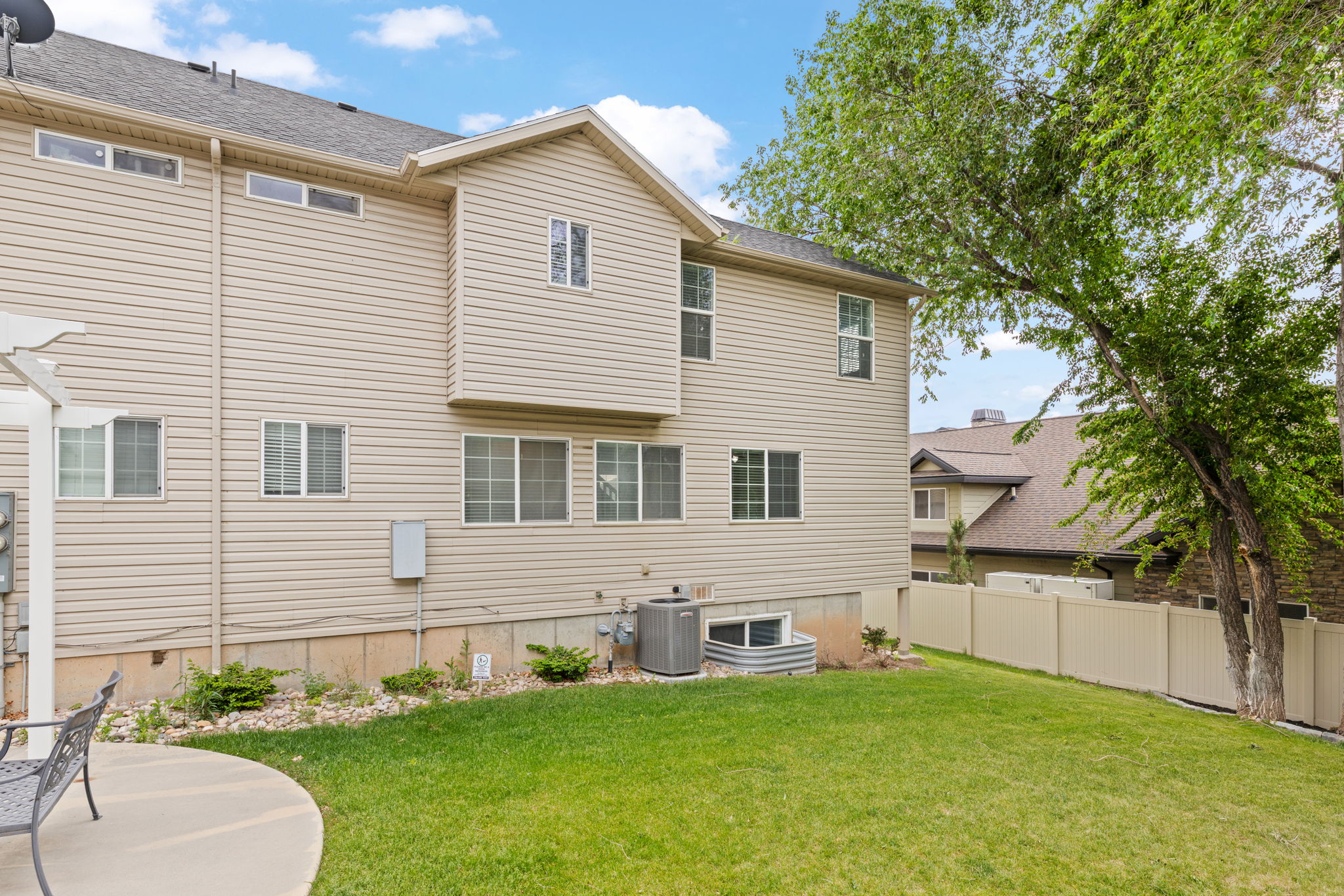 Exterior area behind home, common space with grass, mature trees, and flower beds