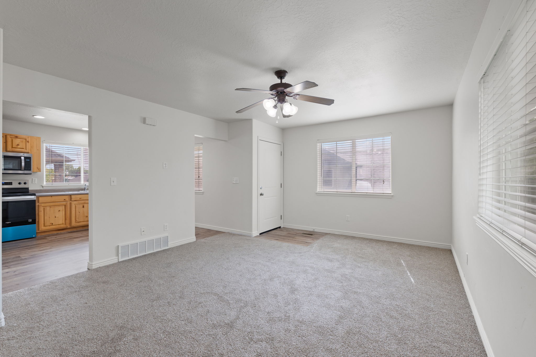 Spacious carpeted living room with fresh neutral paint and abundant natural light, open to the kitchen