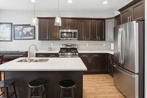 Modern kitchen featuring dark wood cabinetry, stainless steel appliances, a subway tile backsplash, and light wood-finish flooring