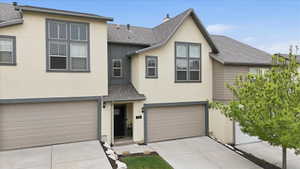 Multi-level townhome featuring a stucco and siding exterior, dual garage doors, and an arched entry with a dark-paneled front door