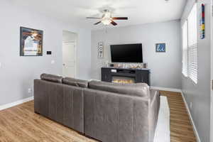 Living area featuring wood-finish flooring, light grey wall paint, and a ceiling fan with integrated lighting