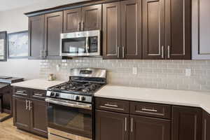Kitchen featuring dark wood-finish cabinetry, light-colored countertops, stainless steel appliances, a gas range, and a subway tile backsplash