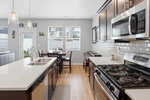 Modern kitchen featuring wood-finish flooring, white countertops, dark wood cabinetry, stainless steel appliances, and a subway tile backsplash