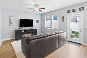 Bright living space featuring wood-finish flooring, an electric fireplace with media console, a ceiling fan with light fixture, and multiple windows