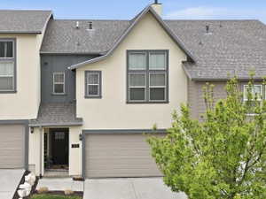 Contemporary townhome exterior featuring a neutral stucco and siding facade, contrasting dark trim, and a two-car garage with a light brown door