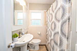 Pedestal sink with chrome faucet, a window with frosted glass, and tiled walls around the tub/shower area