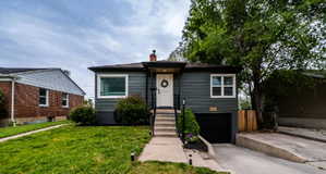 Front exterior featuring dark gray siding, a white front door, a concrete walkway, and a lower-level garage with a black door