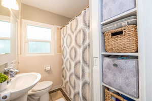 Full bathroom featuring a pedestal sink, a toilet, a privacy window, a tub/shower with a patterned curtain, and built-in shelving
