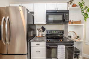 Kitchen featuring a stainless steel refrigerator, white cabinetry with black hardware, stone-look countertops, a black electric range, and an over-the-range microwave