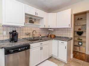 Kitchen featuring white cabinetry, stone-finish countertops, subway tile backsplash, and a stainless steel dishwasher